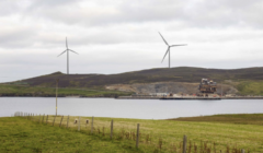 Wind turbines on a hill next to a body of water.