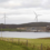 Wind turbines on a hill next to a body of water.