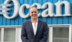 A man in a suit standing in front of an ocean sign.