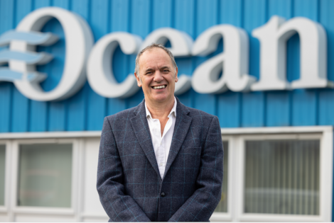 A man in a suit standing in front of an ocean sign.