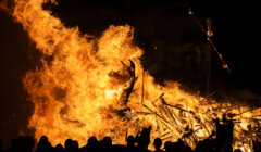 A group of people watching a bonfire at night.