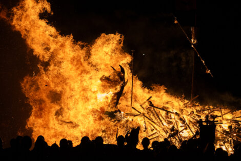 A group of people watching a bonfire at night.