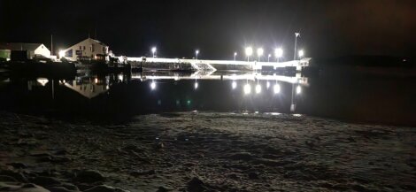 A dock is lit up at night with a boat in the water.