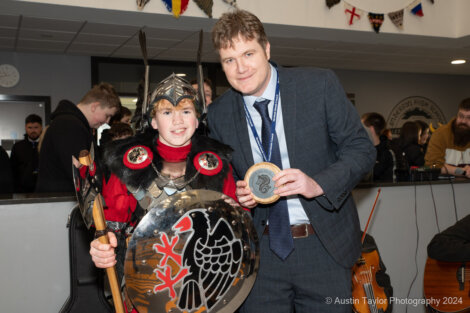 A man in a suit is standing next to a boy with a shield.