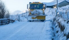 A snow plow driving down a snow covered road.