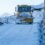 A snow plow driving down a snow covered road.