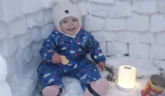 A baby sitting in the snow with a candle.