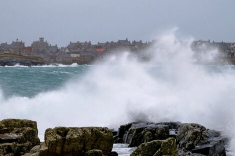 Waves crashing waves on rocks by a town with niagara falls in the background.