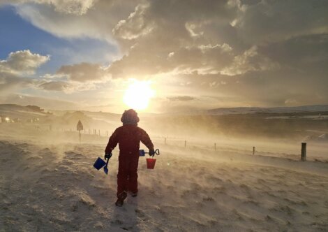 A child in a red suit walking down a snowy hill.