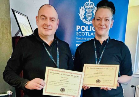 Two police officers holding certificates in front of a banner.