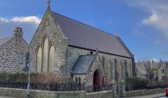 A red car is parked in front of a church.