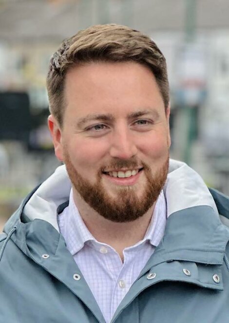 A man with a beard smiling in a blue jacket.