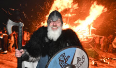 A man in viking costume standing in front of a bonfire.