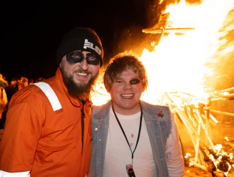 Two men standing next to a bonfire.