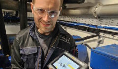 A man holding a tablet in front of a machine.