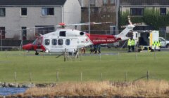 A white and red helicopter parked next to a body of water.