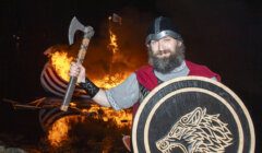 A man in a viking costume standing in front of a fire.