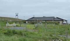 A house with a fence in the middle of a grassy field.