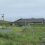 A house with a fence in the middle of a grassy field.