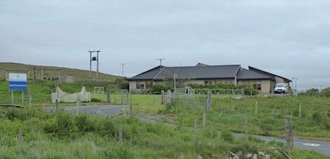 A house with a fence in the middle of a grassy field.