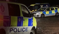 Two police cars parked on a muddy road at night.