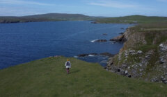 A person is standing on a grassy hill overlooking the ocean.