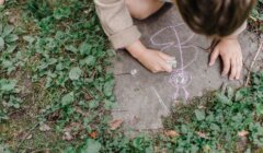 A child drawing on a rock in the grass.