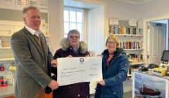 Three people standing in front of a store with a check.