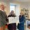 Three people standing in front of a store with a check.