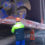 A worker in a high-visibility jacket observes a large ship's propeller being hoisted by a crane in a dry dock facility.