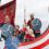 A family dressed as vikings with shields and a spear aboard a boat float with a dragon head design during a parade.