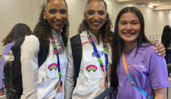 Three smiling individuals posing for a photo, two wearing matching uniforms with medals and one in a lavender shirt.