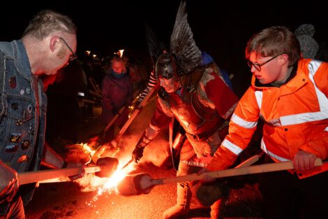 People attending a fire-lighting ceremony with a person dressed in historical armor.