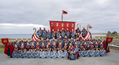 Group of people in viking reenactment attire posing with shields and flags.