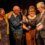 Four individuals on stage celebrating with a trophy, conveying a sense of camaraderie and achievement.