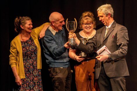 Four individuals on stage celebrating with a trophy, conveying a sense of camaraderie and achievement.