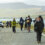 Group of hikers walking along a single-track road near a coastal area with a warning sign advising to reduce speed now.