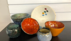 A collection of colorful ceramic bowls and a plate with decorative patterns displayed in front of a stack of white books.