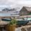 Old wooden boat and stacked stones in the foreground with a large cruise ship anchored in the bay beyond, viewed from a coastal village.