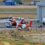 Two helicopters on a tarmac near an airport building with ground support equipment in the vicinity.