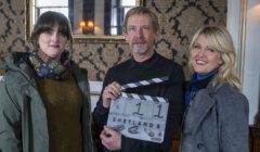 Three individuals on a film set, one holding a clapperboard with the title "shetland," poised for a scene.