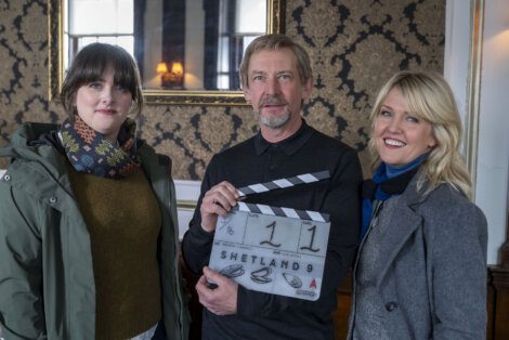 Three individuals on a film set, one holding a clapperboard with the title "shetland," poised for a scene.