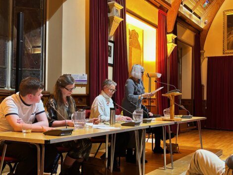 Panel discussion in an ornate room with a speaker at the podium and attentive panelists.