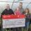 A group of people holding a check in front of a greenhouse.