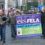 A group of demonstrators marching on a street, led by a bagpiper, while carrying a banner for the further education lecturers' association advocating for unity and strength.