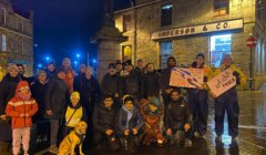 Group of people gathered at night for an event, holding signs with messages of solidarity and peace.