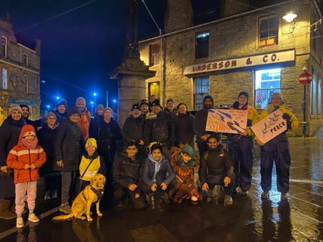 Group of people gathered at night for an event, holding signs with messages of solidarity and peace.