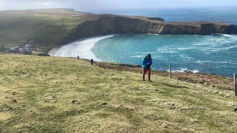 A person standing on a grassy cliff overlooking a bay with turquoise waters.