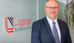 Professional in a suit posing in front of a loganair sign.