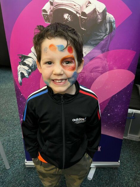 A young boy with paint on his face standing in front of a poster.